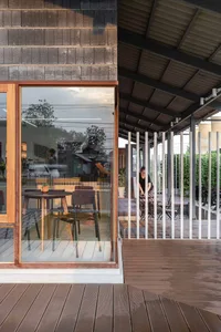 A cafe exterior featuring wooden windows and a tiled roof, with a person working near the entrance.