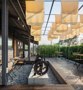 An industrial-style outdoor seating area with fabric canopies, wooden chairs, and concrete flooring.