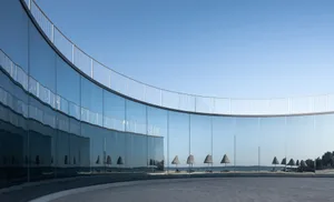 A modern, curved glass installation reflecting a beach scene and beach huts.