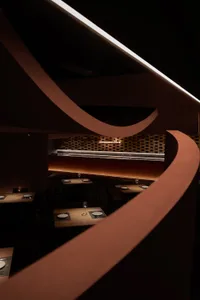 A modern restaurant interior with wooden tables, chairs, and a warm, ambient light from a linear chandelier.