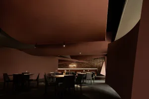 Interior of a modern restaurant with minimalist design, featuring wooden tables, brick walls, and metallic accents.
