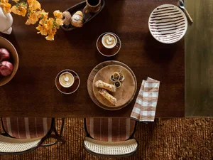 A wooden breakfast table set for coffee and pastries in a rustic interior design setting.