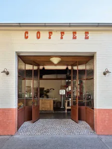 A cozy coffee shop exterior with brick and concrete materials, open doors revealing a welcoming interior.