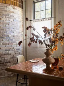 A modern, industrial-style interior with concrete and brick surfaces, a tile table, and a decorative plant vase.