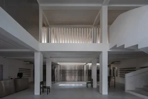A minimalist industrial storefront with concrete walls and floors, white columns, and a mezzanine level with metal railings.