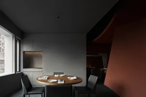 Modern minimalist restaurant dining room with a round wooden table, black leather chairs, and sleek metal accents.