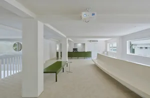 A modern office space featuring white concrete walls, a green reception desk, and minimalist furniture.