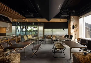 Contemporary restaurant interior featuring cement walls, wooden tables, and black metal chairs.