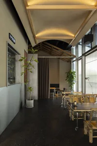 A restaurant interior featuring wood and concrete materials with large windows and industrial-style lighting.