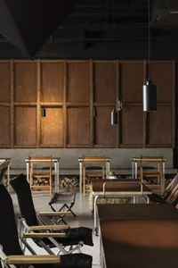Large, cozy cafe interior featuring wooden tables, concrete walls, metal accents, and fabric seating.