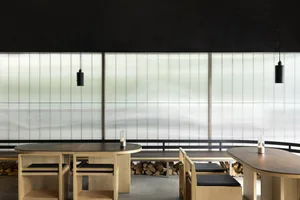A modern restaurant interior featuring wooden furniture, glass elements, and a concrete floor.