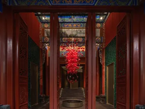 A red metallic chandelier hanging from the ceiling in a stylish interior design setting.