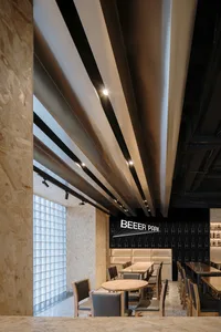 A modern industrial restaurant interior with a metal beam ceiling, wooden tables, and sleek black accents.