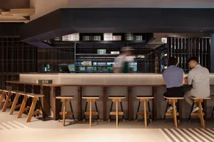 Industrial-style restaurant bar counter featuring wooden stools and shelves with boxes.