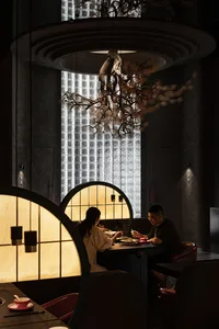 A modern restaurant interior with wooden seating, warm lighting, and concrete walls.