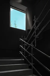 Industrial-style staircase with metal handrails and black walls, featuring a window with a view of the sky.