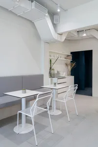 Modern coffee shop interior with metal tables and chairs, grey fabric seating, and minimalist decor.