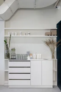 A sleek, modern coffee shop counter with white materials and minimalistic design, featuring coffee cups, glasses, and utensil