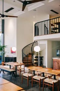 Industrial-style restaurant interior with wooden tables, metal chairs, and spiral staircase.