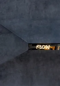 A minimalist concrete interior design with the word 'FLOW' illuminated.