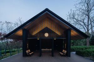 A modern architectural structure featuring a black wooden exterior with illuminated wood slats and seating area.