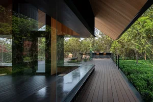 Modern exterior building with glass walls and wooden structures surrounded by greenery.