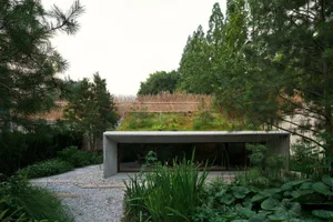 Modern minimalist building with green roof surrounded by lush vegetation and concrete pathways.