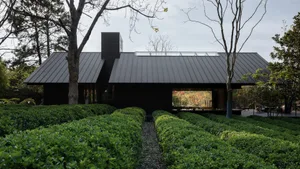 A modern residential building with metallic exterior and greenery surrounding it.