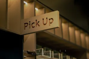 A wooden sign with the text 'Pick Up' hanging from a ceiling.