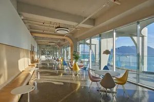 Industrial-themed coffee shop with steel furniture and large windows overlooking a scenic view of mountains and water.