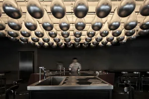 A minimalist bar with metal and concrete finishes and a modern lighting installation featuring hanging glass elements.