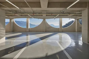 A spacious, modern parking garage interior with concrete walls and arched windows overlooking the ocean.