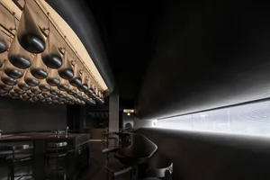Minimalist design featuring modern restaurant interior with hanging silver light fixtures in a black space.