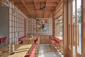 A modern restaurant interior featuring wooden furniture, a colorful mural, and red seating.