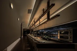 Long, open industrial restaurant bar with wood stools and hanging lights.