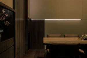 A minimalist dining area with wooden table and leather chairs, illuminated by hidden lighting under the wall.