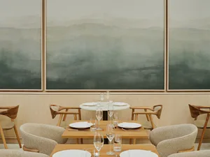 A minimalist restaurant interior with wooden tables, chairs, and abstract wall art.