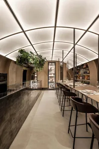 Interior of a modern bar with concrete walls, glass railings, and a high ceiling.