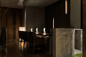 A modern minimalist dining room with wooden floors, stone walls, and wooden chairs and tables.