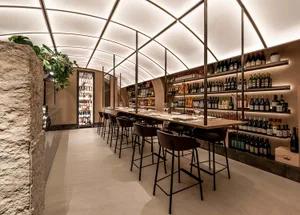 A modern restaurant bar with high ceilings, glass walls, and stone accents.
