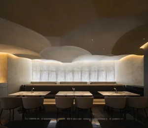 A modern restaurant interior with concrete walls, lit by warm, ambient lighting.