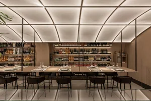 A spacious and contemporary restaurant interior featuring a large dining table surrounded by chairs and a well-stocked wine b