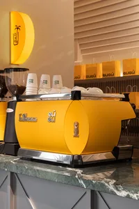 A bright yellow espresso machine sitting on a green marble counter.