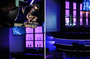 A modern, industrial-style bar with metal and glass elements, illuminated by neon lights.