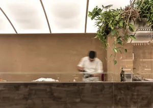 A sleek, modern restaurant kitchen featuring exposed concrete walls and a glass front counter.