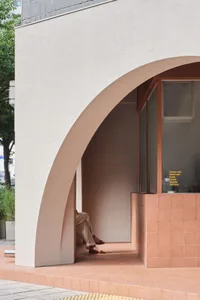 A woman sitting in a modern minimalist entrance made of concrete.