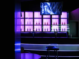 Modern bar interior with purple LED lights and illuminated shelving displaying bottles of alcohol.