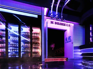 A modern bar restaurant entry with glass refrigerators filled with drinks and a concrete floor.