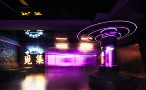 An industrial-style nightclub/lounge interior with modern metal fixtures and vibrant neon lighting.