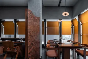 A modern restaurant interior with brown leather chairs, wooden tables, and metal pendant lights.